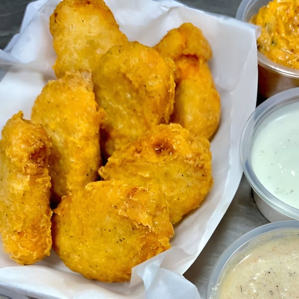 Golden-fried seafood nuggets in a white paper-lined basket, with three dipping sauces in plastic cups.