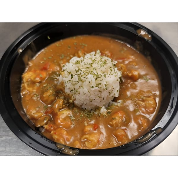 A black bowl of DaDam Crab seafood gumbo with rice and herbs on a metal surface.