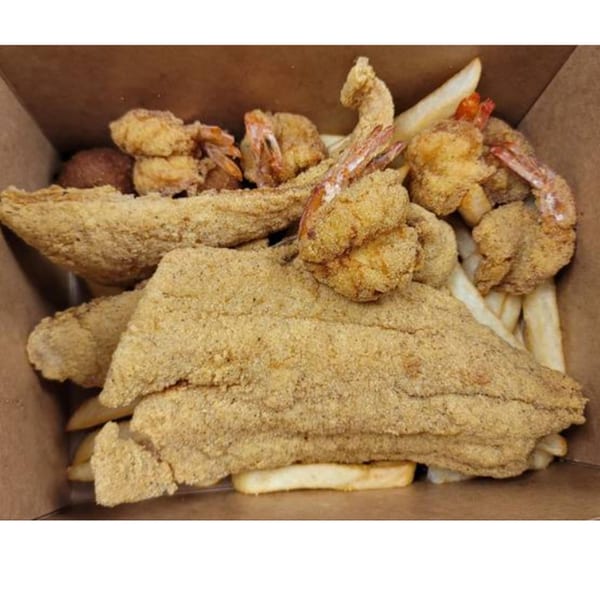 A cardboard box filled with crispy fried fish fillets, shrimp, hushpuppies, and french fries.
