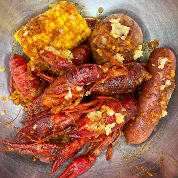 A metal bowl filled with DaDam Crab's crawfish, corn on the cob, potatoes, and sausage, all seasoned.