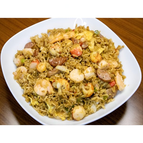 A white plate filled with seafood fried rice, shrimp, sausage, and egg on a wooden table.