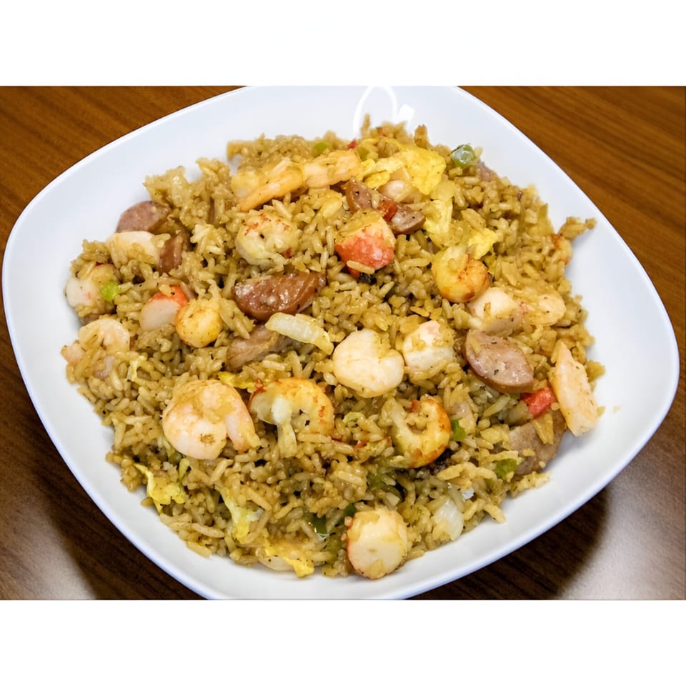 A white plate filled with seafood fried rice, shrimp, sausage, and egg on a wooden table.